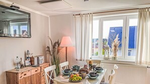 A dining area with a table set for four, a wooden cabinet, and a window with curtains. - Beautiful apartment for 6 people with WIFI, TV and patio (Ostseebad Kühlungsborn)