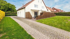 A two-story house with a paved driveway and a wooden fence. - Beautiful apartment for 6 people with WIFI, TV and patio (Ostseebad Kühlungsborn)