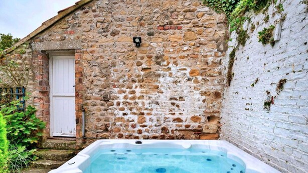 A stone building with a white door and a hot tub in front.