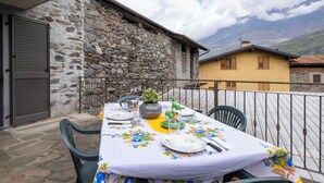 An outdoor dining area with a stone wall, a yellow building, and a mountain view. - Wonderful private villa for 4 guests with WIFI, TV, terrace and pets allowed (Talamona)