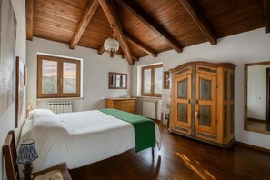Een slaapkamer met een houten plafond, een bed met een groene deken, een houten kledingkast en een radiator.