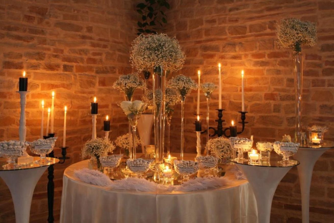 A table set with candles, glassware, and floral arrangements against a brick wall.