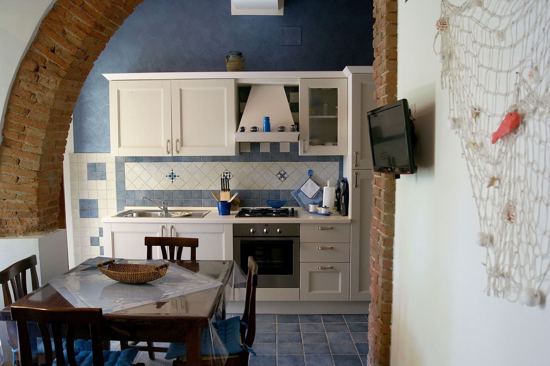 A kitchen with white cabinets, a tiled backsplash, a gas stove, and a TV mounted on the wall.
