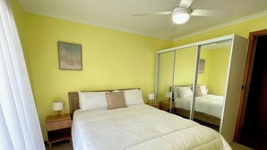 Quarto com uma cama grande, um ventilador de teto, um espelho e uma mesinha de cabeceira com abajur.