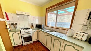 Cozinha compacta com armários brancos, fogão a gás, micro-ondas, torradeira e janela com vista para o exterior.
