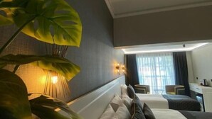 A hotel room with a bed, bedside tables, a desk, and a large plant. - PARK MİLANO (Izmir)