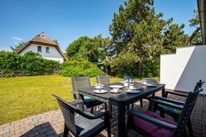 A patio with a table set for dining, surrounded by chairs, in a garden with a house in the background. - Terraced house in a quiet location close to the beach (Wustrow)