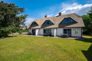 A two-story house with a sloped roof, a patio with outdoor furniture, and a stone wall in the background. - Terraced house in a quiet location close to the beach (Wustrow)
