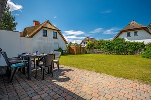 A patio with a table and chairs, a brick pathway, and two white houses with thatched roofs. - Terraced house in a quiet location close to the beach (Wustrow)
