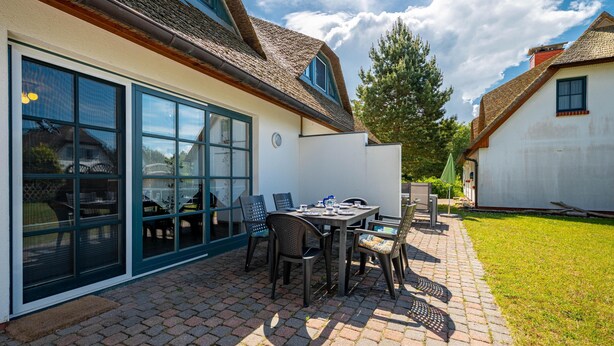 A patio with a table and chairs, a covered outdoor seating area, and a building with large windows and a sloped roof. - Terraced house in a quiet location close to the beach (Wustrow)