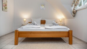 A neatly made bed with two pillows and two folded towels, a small bedside table with a lamp, and a window with curtains. - Terraced house in a quiet location close to the beach (Wustrow)
