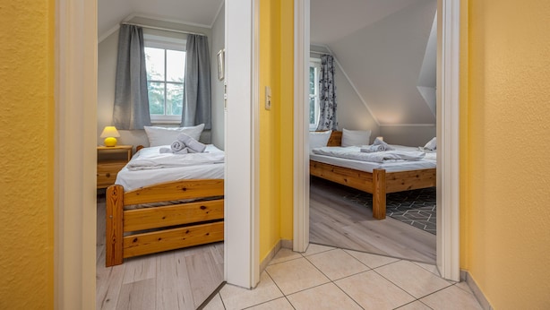 Una camera da letto con due letti in legno, un comodino con lampada, una finestra con tende e una porta che dà su un'altra stanza.