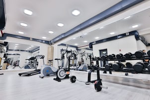 A gym with cardio machines, weight racks, and a mirrored wall.