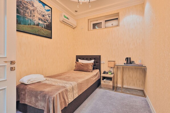 A bedroom with a bed, bedside table, and a small desk with a lamp. - Fergana Hotel (Fergana)