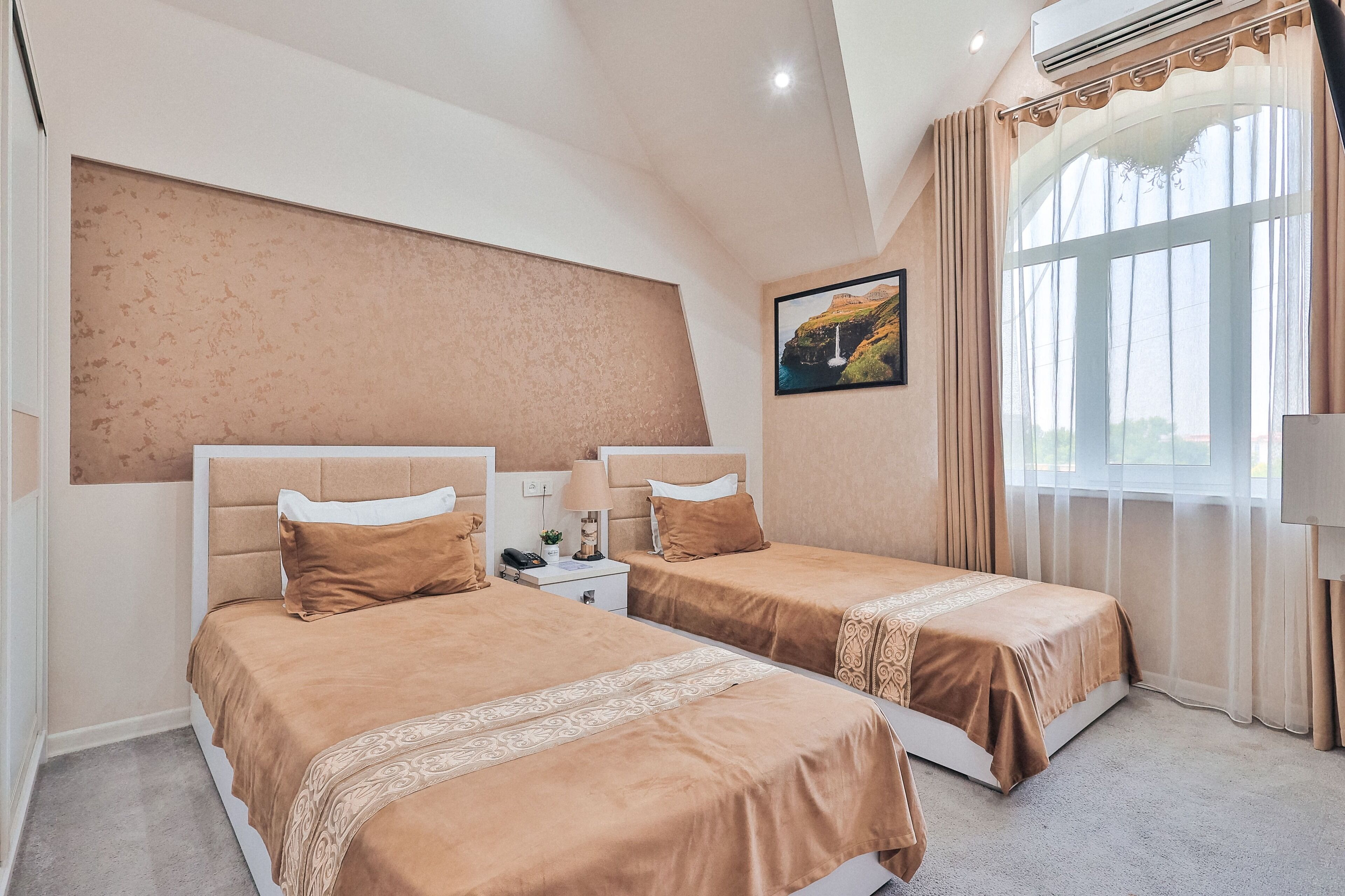 Habitación de hotel con dos camas, un ventanal con cortinas, un cuadro en la pared y un ventilador de techo.