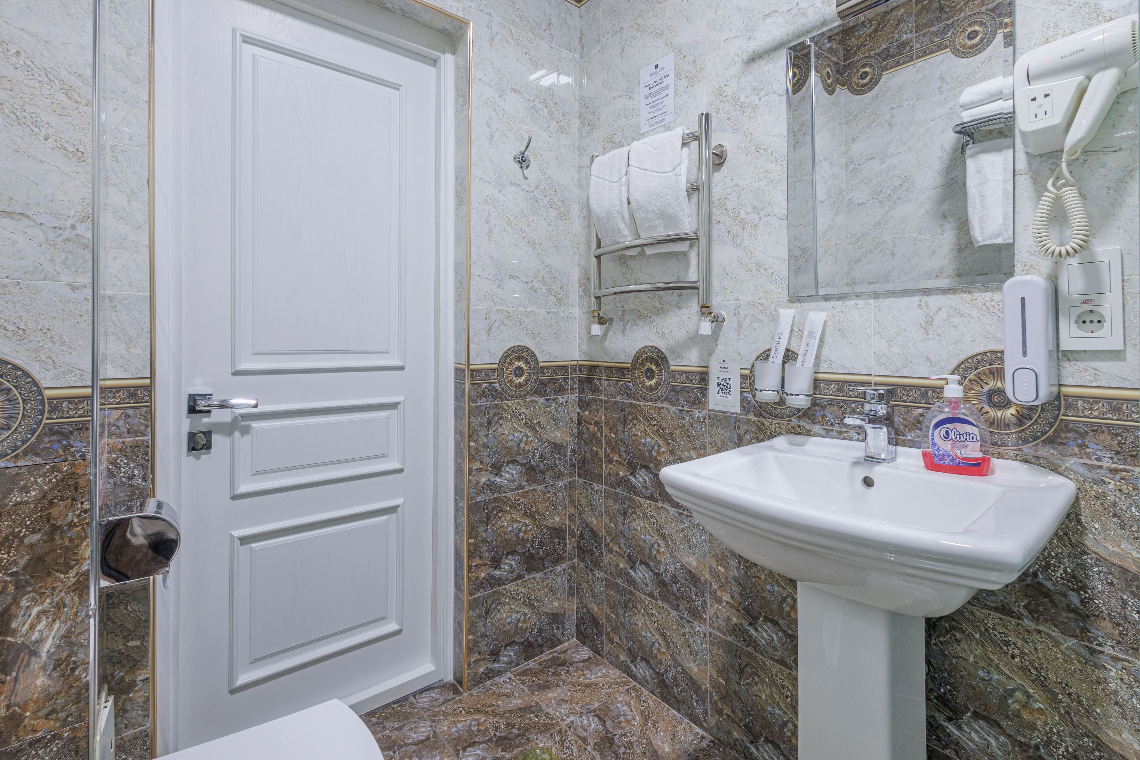 A bathroom with a white door, a sink with a soap dispenser, a towel rack, and a mirror.