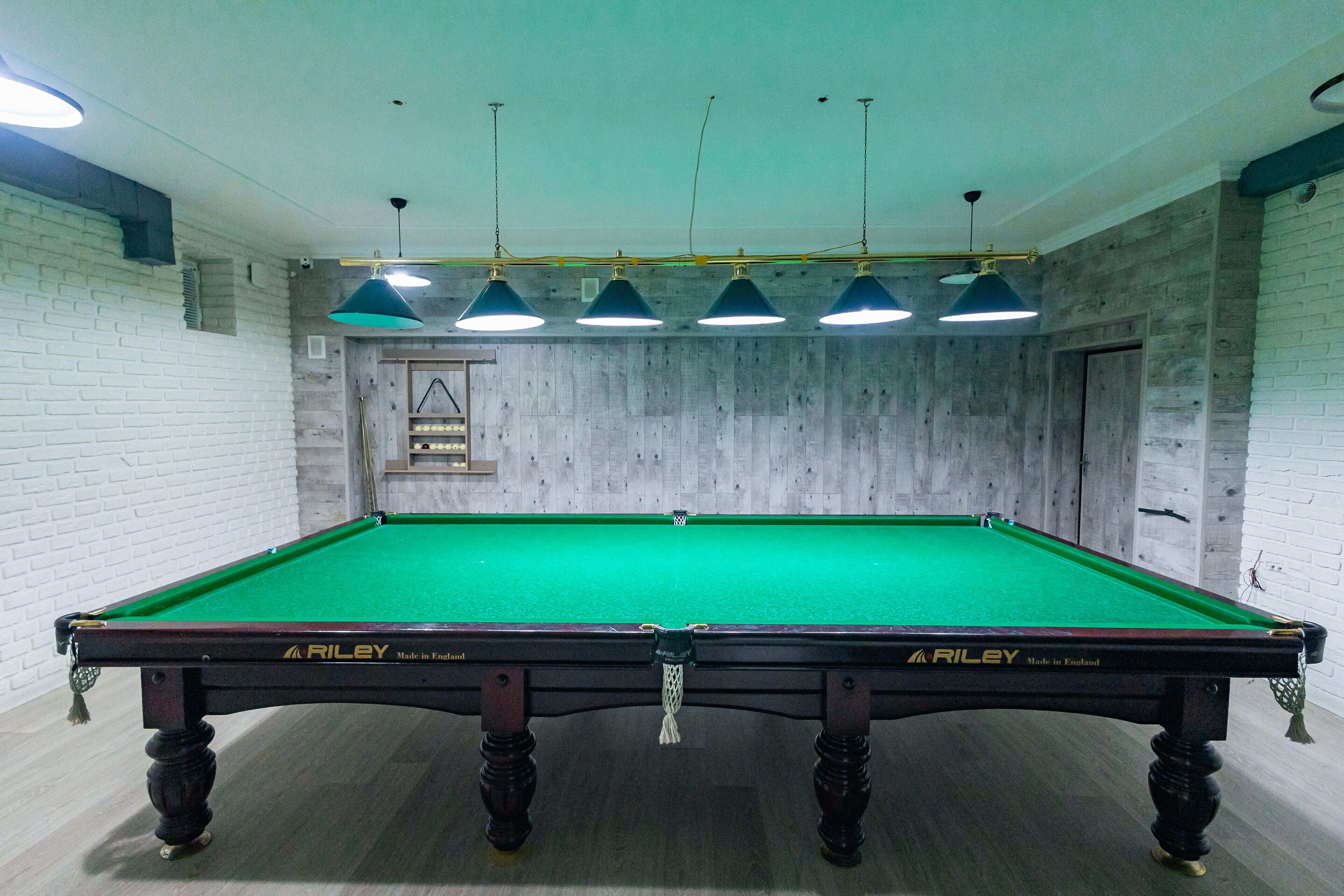 A pool table with a green felt surface, surrounded by a brick wall and wooden paneling.