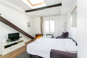 A bedroom with a bed, a television on a white stand, a chest of drawers, a window, and a skylight. - Stylish 1BR in the Heart of Le Marais (Paris)