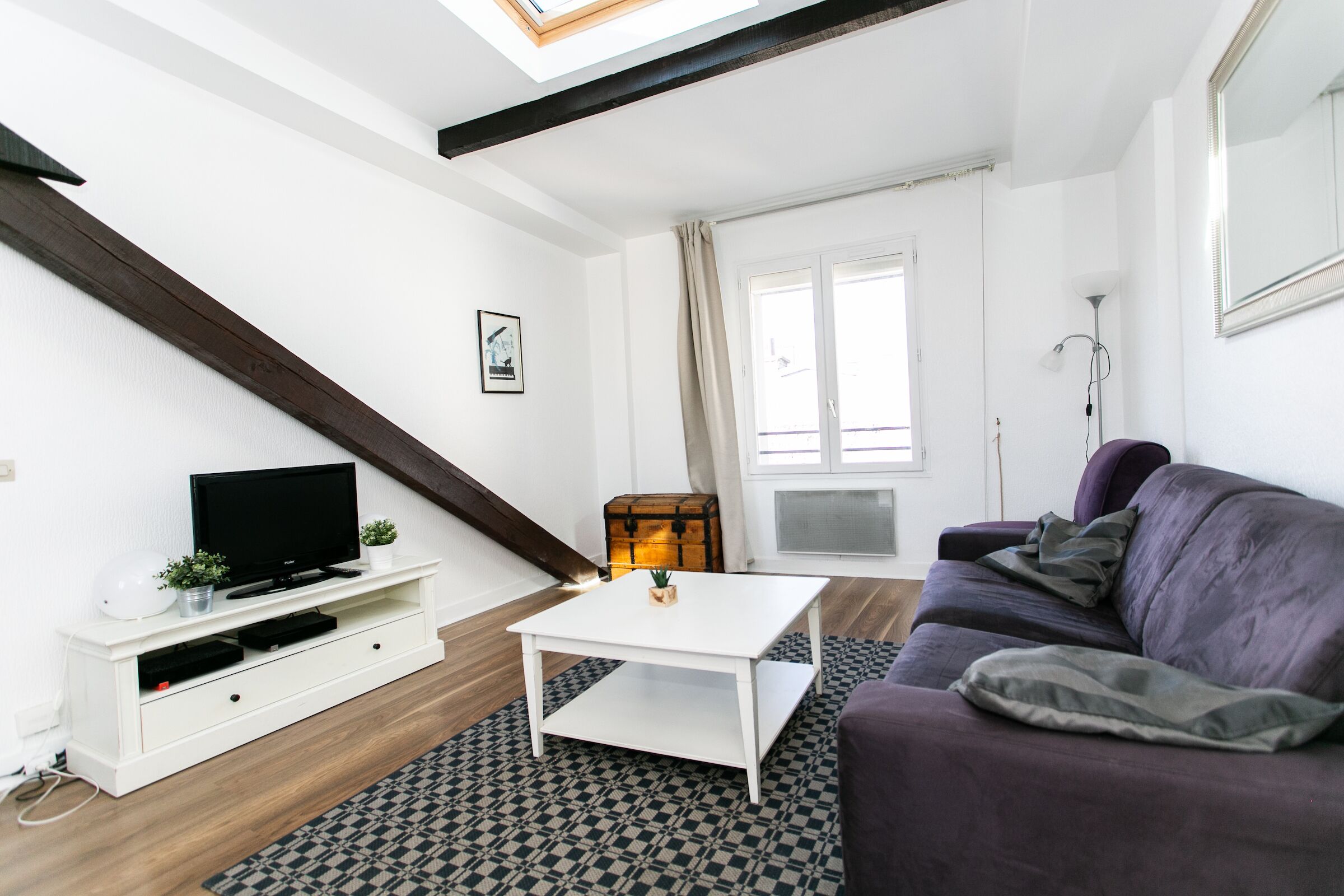A modern living room with a white TV stand, a white coffee table, a purple sofa, and a patterned rug.