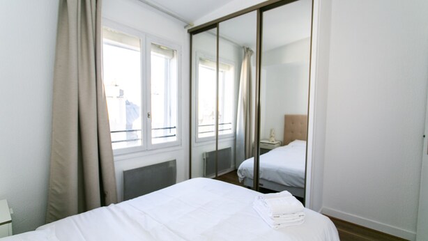 A hotel room with a bed, a large mirror, and a window with curtains. - Stylish 1BR in the Heart of Le Marais (Paris)