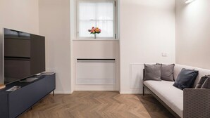 Ett modernt vardagsrum med en platt-TV, en soffa och ett fönster med en blomsteruppsättning.