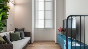 En moderne stue med sofa, stort vindue, blå skab og en plante.