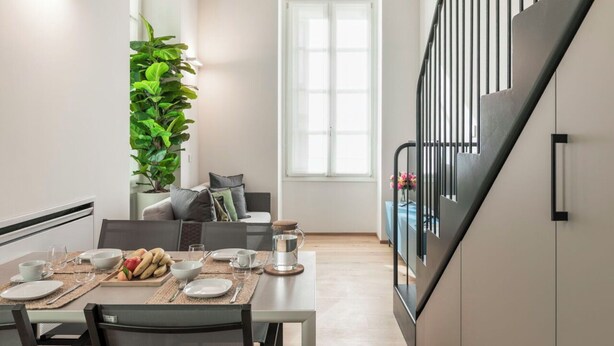 Et moderne spiseområde med et bord dækket til to personer, en potteplante og udsigt til trappen.