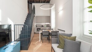 Et moderne interiør med trappe, spiseplads og opholdsområde med fjernsyn og skrivebord.