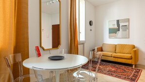 Ein modernes Wohnzimmer mit einem runden weißen Tisch, transparenten Stühlen, einem gelben Sofa und einem großen Spiegel.