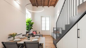 Un coin repas avec une table en bois dressée pour quatre personnes, une plante en pot et un escalier doté d’une rampe noire.