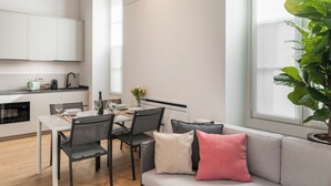 Une cuisine moderne avec des meubles blancs, une table à manger pour quatre personnes et une grande fenêtre donnant sur un paysage verdoyant.