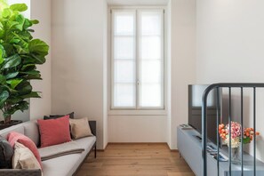 A modern living room with a grey sofa, a large green plant, a window, and a TV stand with a flower vase. - Apartment in Como with 2 bedrooms sleeps 4 (Como)