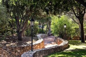 Un chemin de pierres aménagé dans un jardin paysager, avec des arbres et deux lampadaires noirs de style lanterne.
