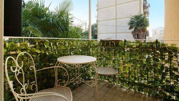 A balcony with a metal table and chairs, a green leafy wall, and a building in the background. - Ca' Mercati Apartment with Two Bedrooms in Mestre Venice (Venezia)
