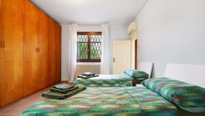 A bedroom with a wooden wardrobe, a window with curtains, a radiator, and a bed with patterned bedding. - Ca' Mercati Apartment with Two Bedrooms in Mestre Venice (Venezia)