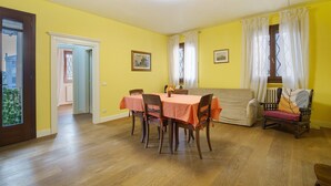 A dining area with a table set for four, wooden chairs, a sofa, and a window with curtains. - Ca' Mercati Apartment with Two Bedrooms in Mestre Venice (Venezia)