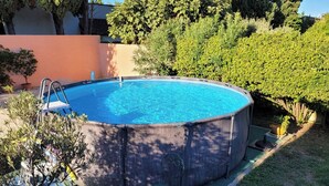 A round above-ground pool with a ladder, surrounded by a grassy area and various plants.