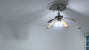 Una habitación con tres camas individuales de madera, piso estampado, ventilador de techo y ventana con persianas azules.
