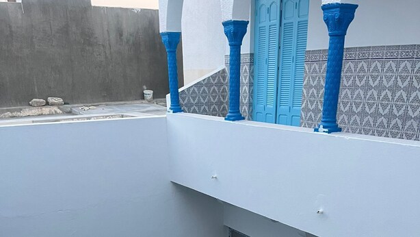 Una piscina en la azotea con una fuente azul, rodeada por un edificio blanco con detalles azules y paredes con mosaicos.