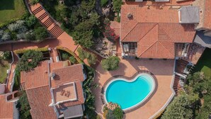 An aerial view of a property with a swimming pool, terracotta-tiled roofs, and landscaped gardens. - Lovely Apartment by the Beach (Arzachena)
