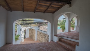 A covered patio with stone walls, wooden beams, and a view of the surrounding landscape. - Lovely Apartment by the Beach (Arzachena)