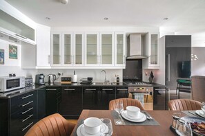 Een moderne keuken met een centraal eiland, zwarte kasten, en een eethoek met bruine stoelen en een tafel gedekt voor twee personen.