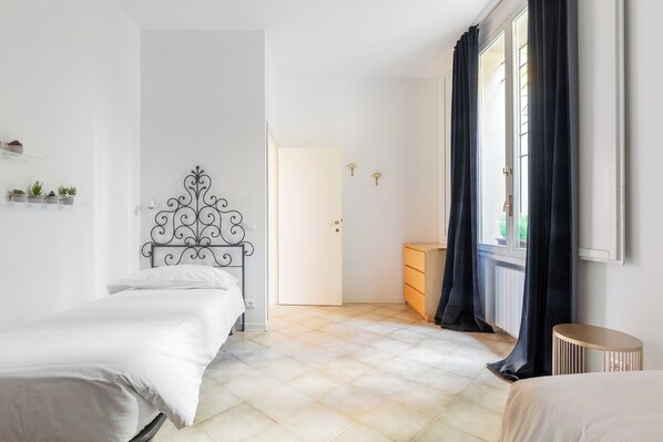 A bedroom with two beds, a wardrobe, a radiator, and a window with curtains. - Gombruti Vintage Apartment by Wonderful Italy (Bologna)
