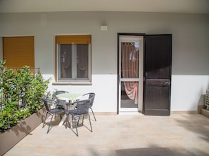 An outdoor patio with a table and chairs, a wooden door, and a window with curtains. - Great Accommodation With a Lovely Patio (Eraclea)