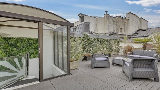 Una terrazza sul tetto con mobili in vimini, una struttura in vetro e vista sugli edifici circostanti.