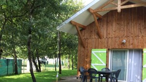 Un bâtiment en bois doté d’un patio couvert, d’une porte verte et d’une table avec des chaises.