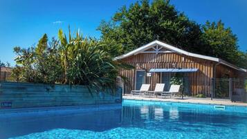 A wooden cabin with a pool, surrounded by lush greenery and trees.