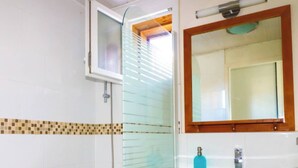 Une salle de bain avec une douche à parois de verre, un meuble-lavabo en bois avec un miroir et un pare-feu en carreaux.