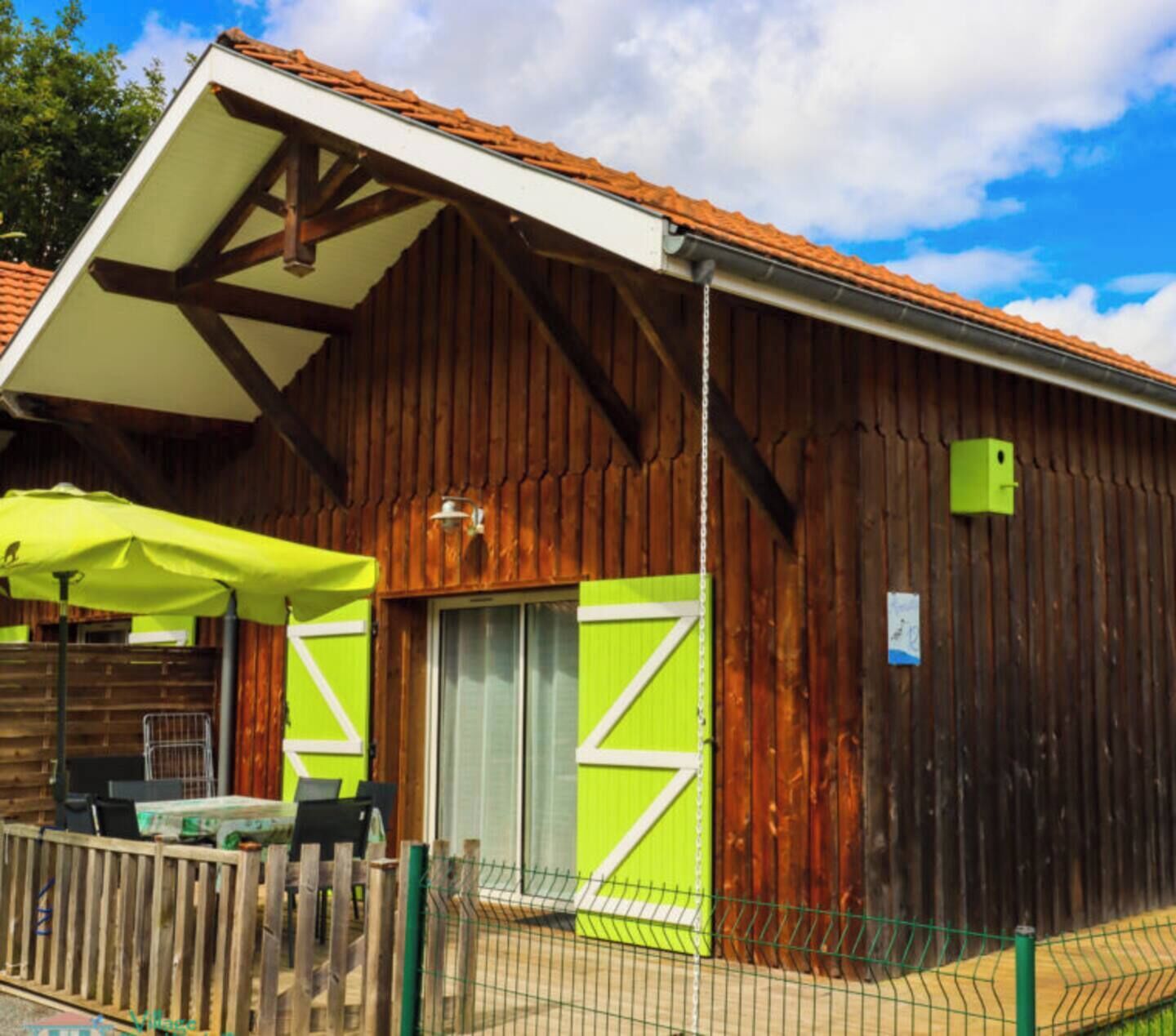 A rustic wooden building with a sloped roof, a green awning, and a fenced outdoor seating area.