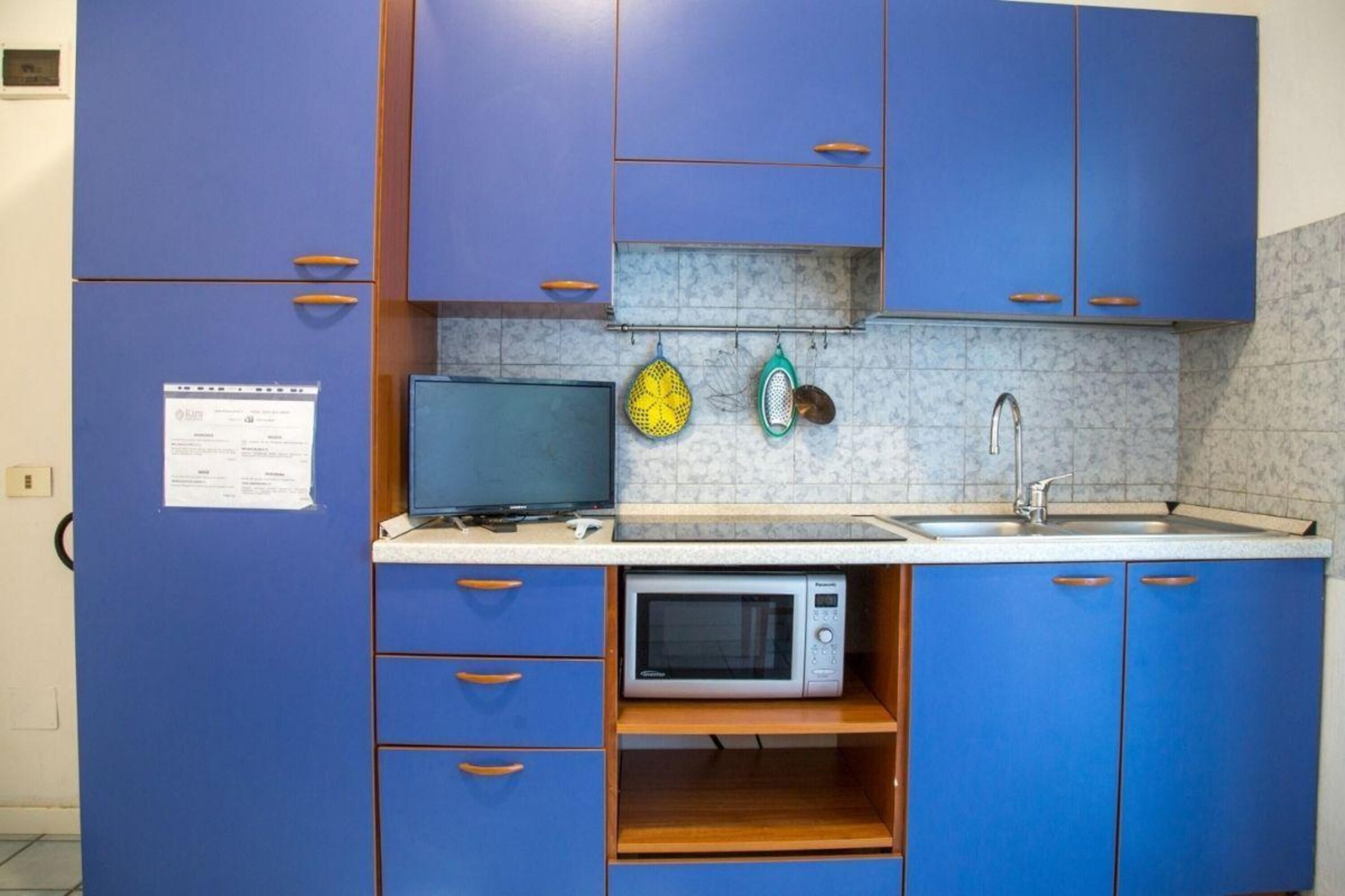 Cozinha compacta com armários azuis, micro-ondas, pia e bancada pequena.